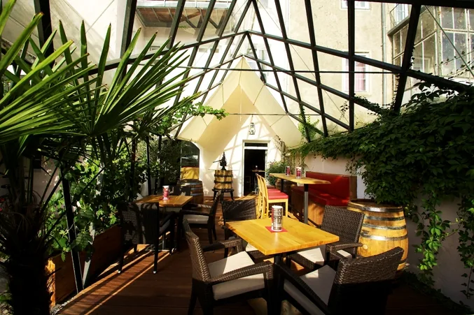 Begrünter Innenhof der kost.bar mit Tischen unter dem Glasdach
