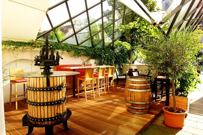 Überdachte Terrasse der kost.bar mit alter Weinpresse und Bartisch
