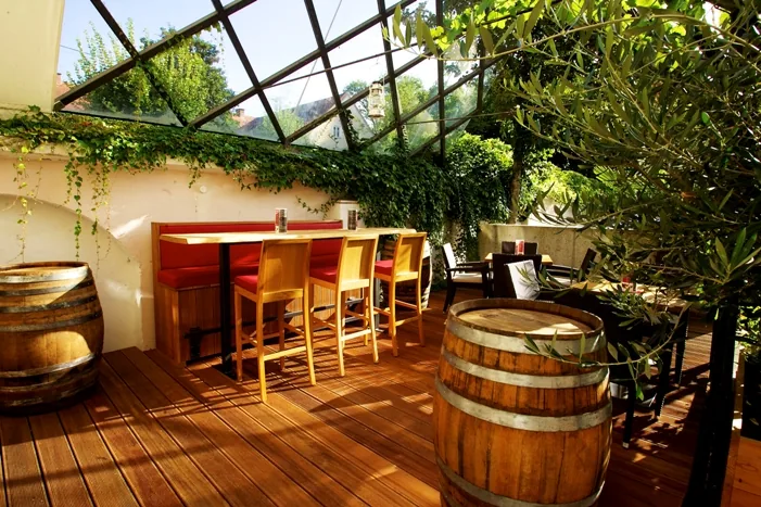 Gastgarten der kost.bar mit Holzfässern, Bartisch und Olivenbäumen